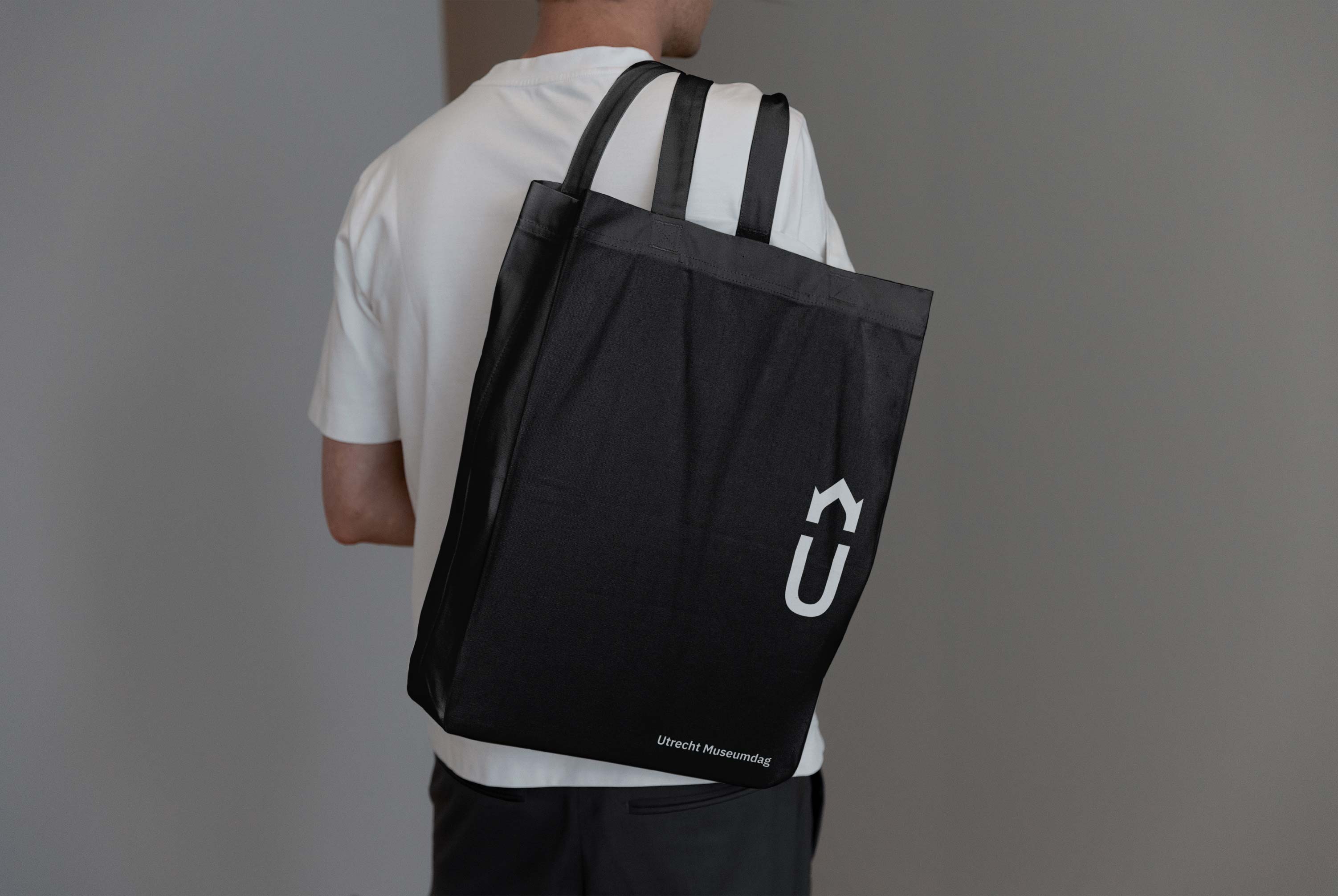 A man carrying a big tote bag over his shoulder with the Utrecht Museumdag logo printed on it